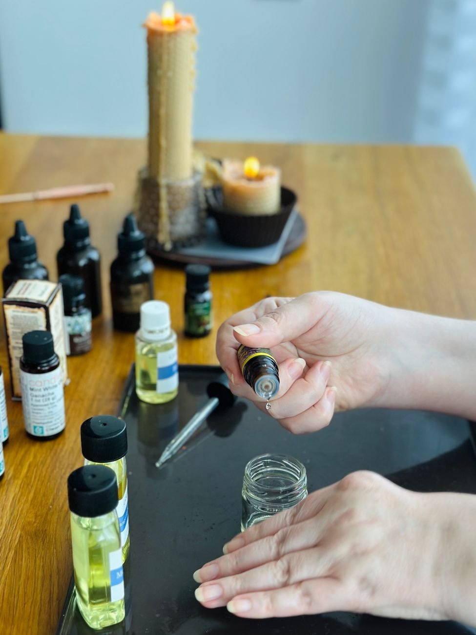 Hands preparing a DIY aromatherapy blend with essential oils and candles on a table.