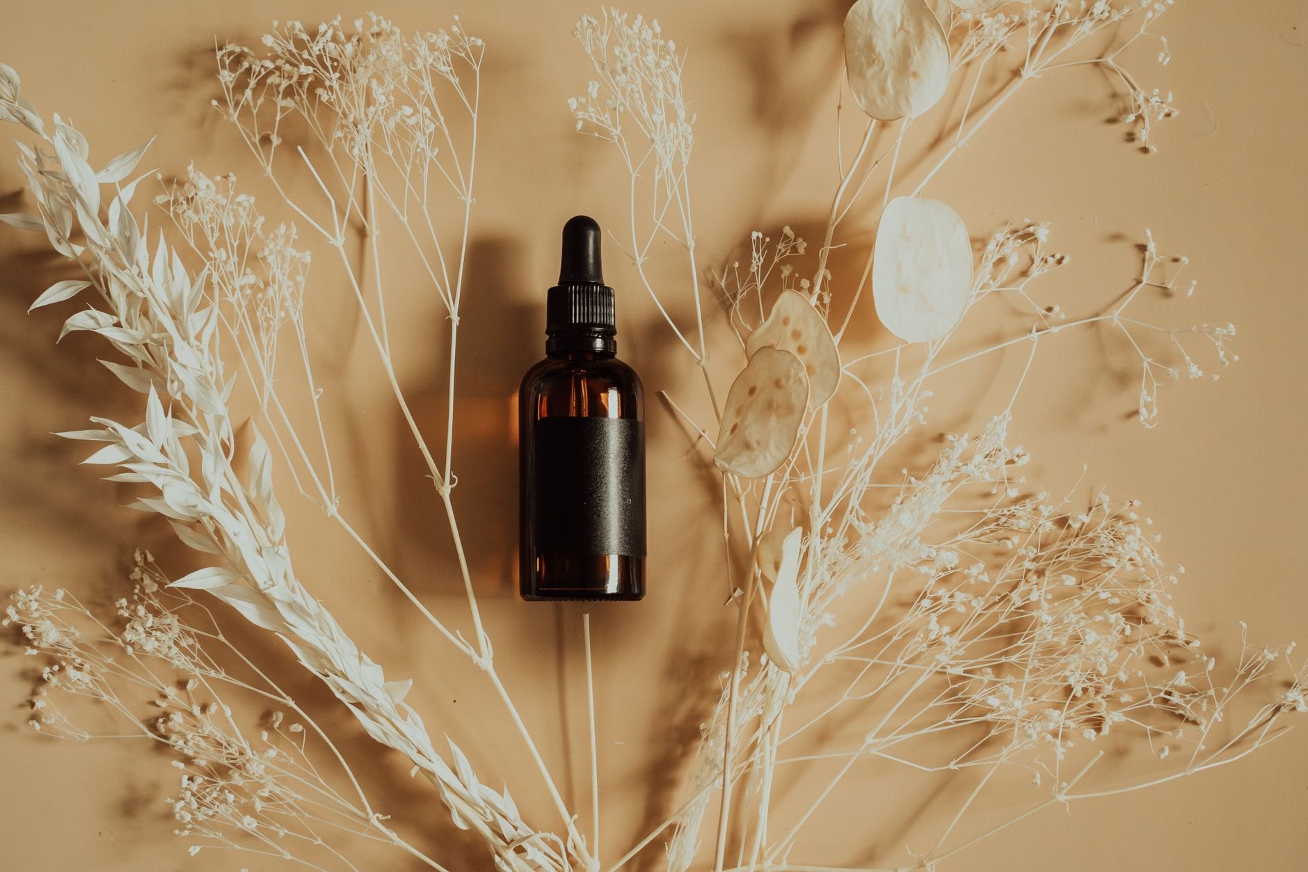 Flat lay of a dropper bottle for essential oils or serums surrounded by dried plants.